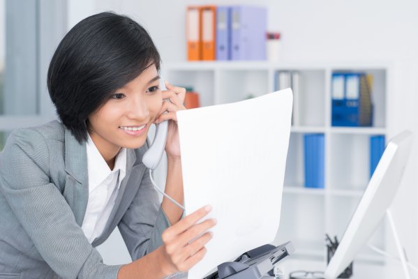 sfax online fax service cost features happy woman on the phone in office holding white papers in hand computer and folders in the background